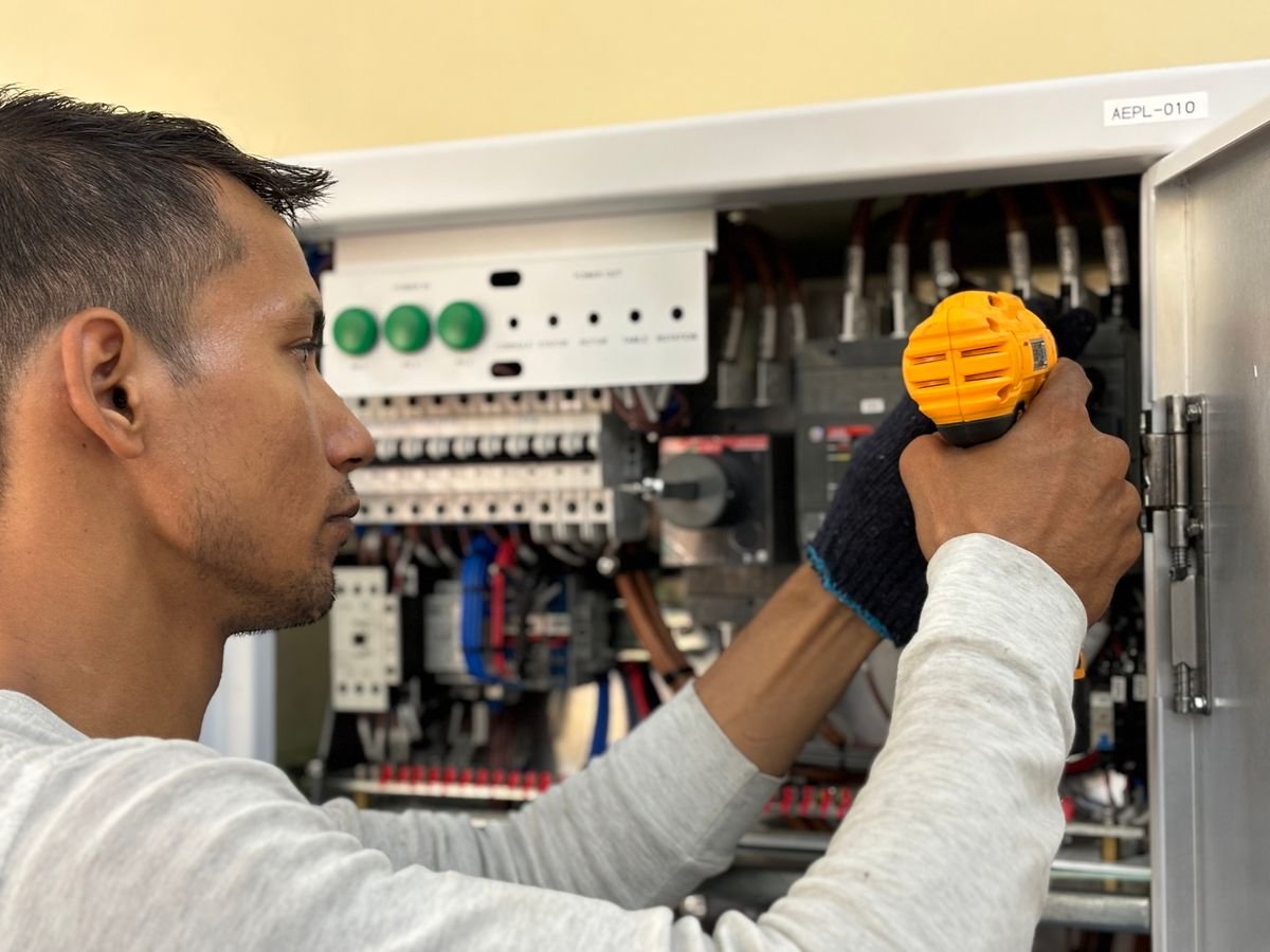 Skilled electrician using a drill to repair electrical equipment indoors