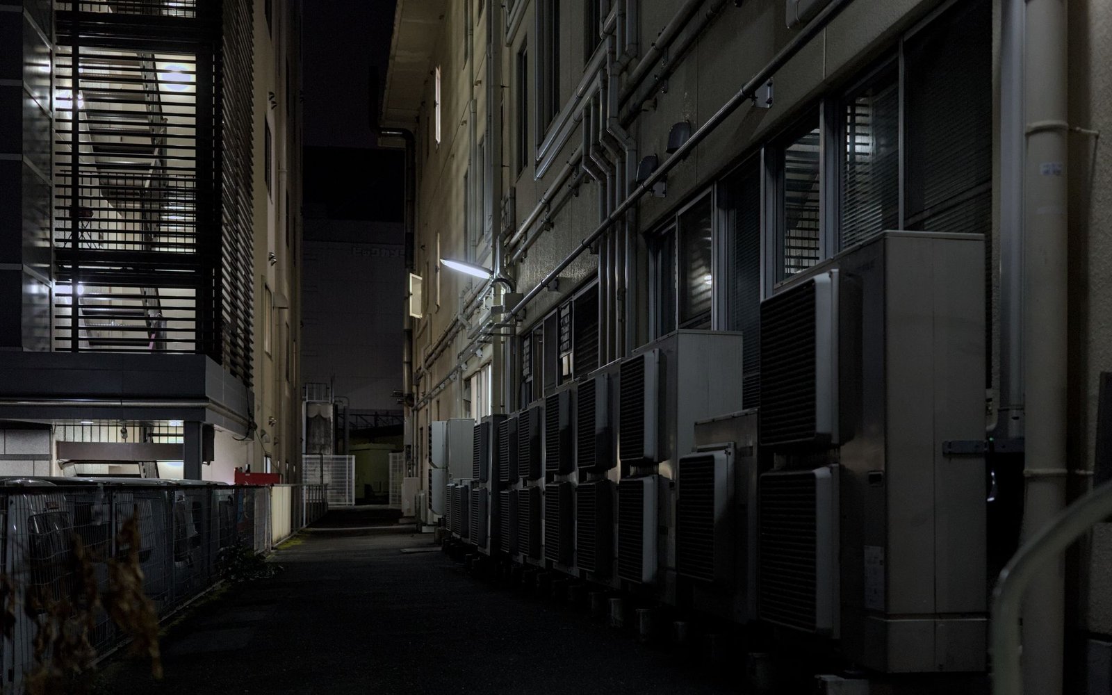 Dimly lit urban alley featuring rows of air conditioning units at night
