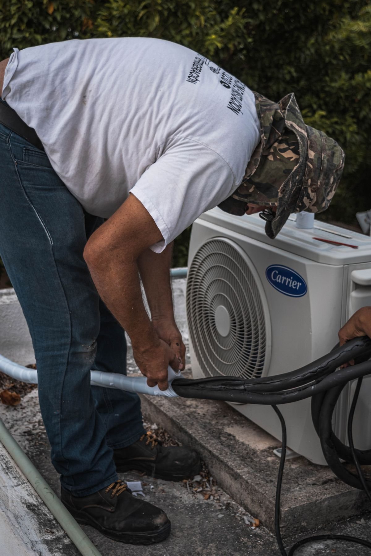Technician performing maintenance on an outdoor air conditioning unit, focusing on hose connections