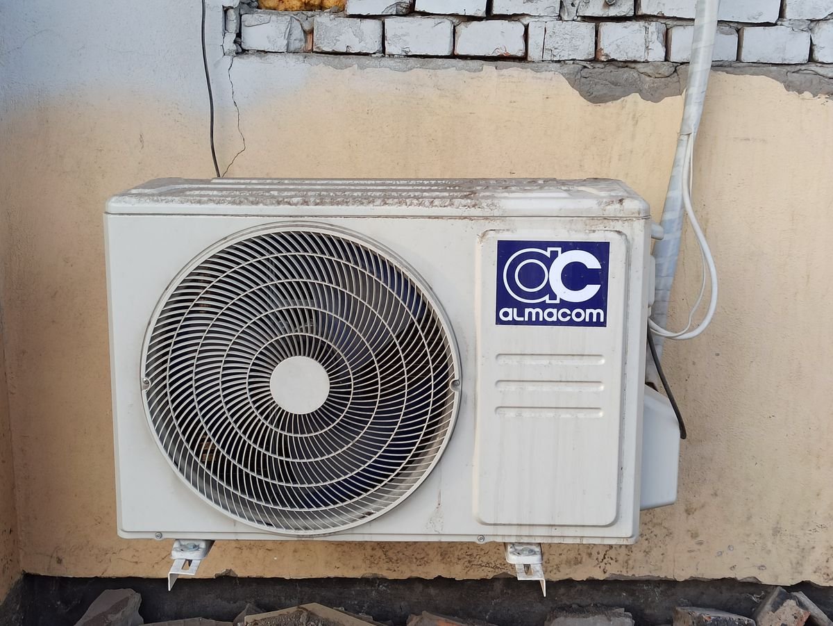 A well-used outdoor AC compressor unit affixed to a brick wall