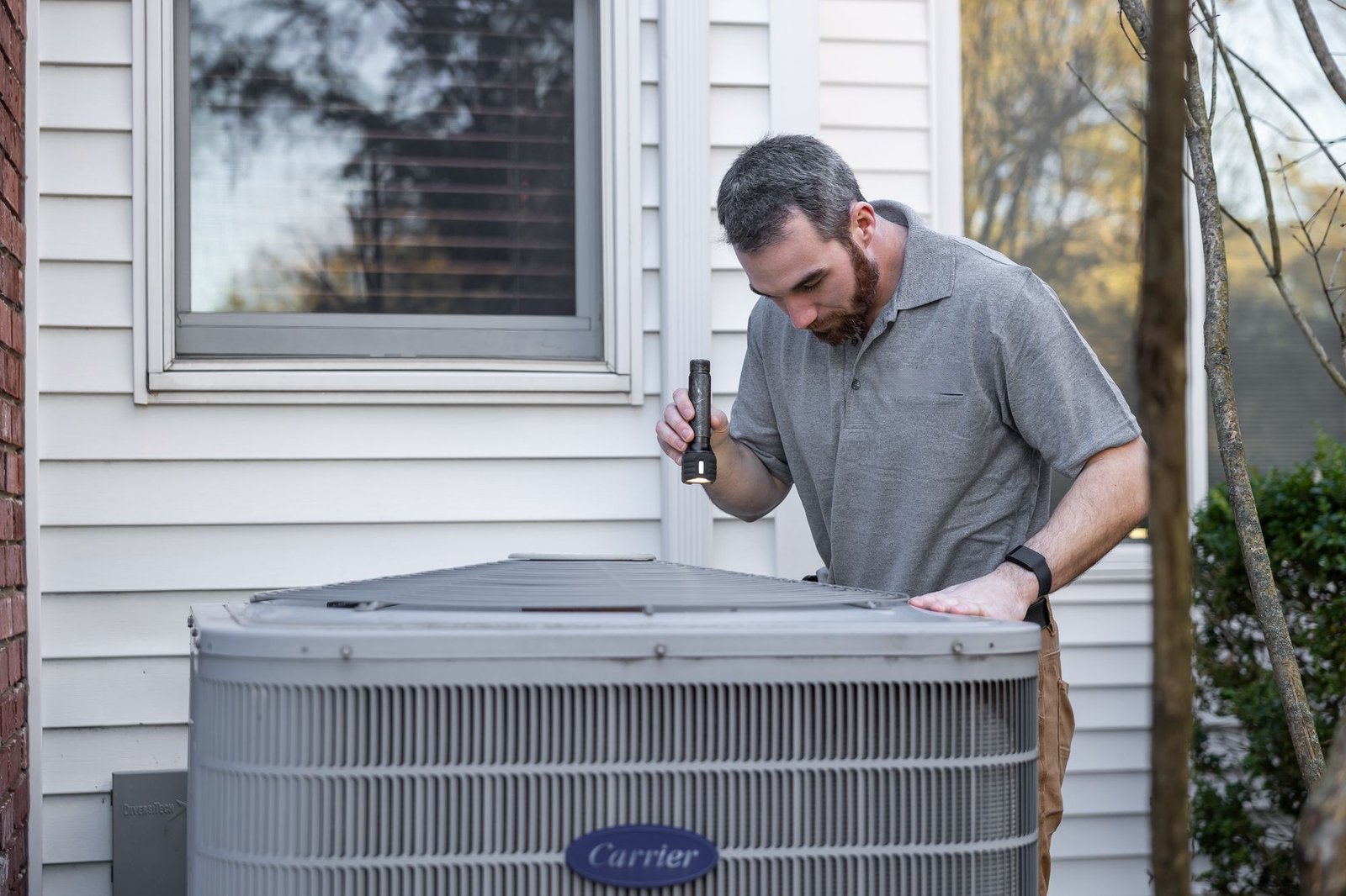 Technician inspecting an outdoor AC compressor unit with a flashlight