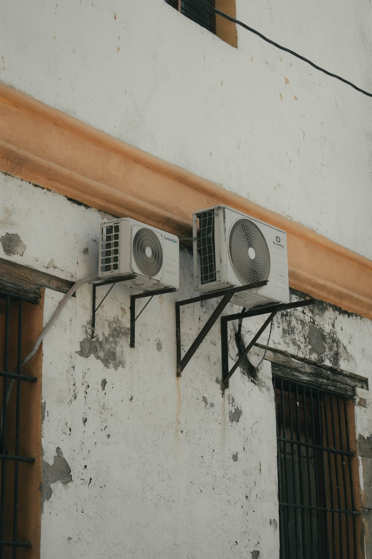 Two outdoor AC compressor units installed on a concrete wall