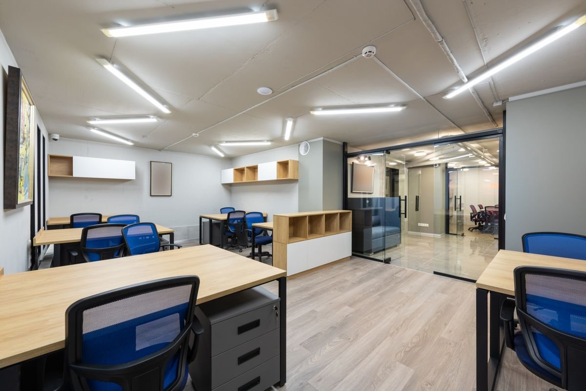 Open office with white ceiling tiles, ducts, and downlights above blue chairs
