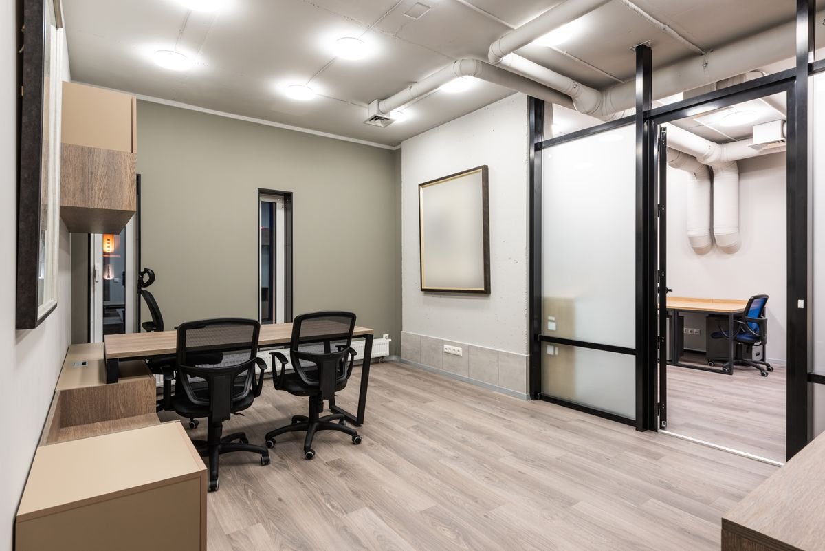 Office rooms divided by black-framed glass partitions with desks and chairs inside