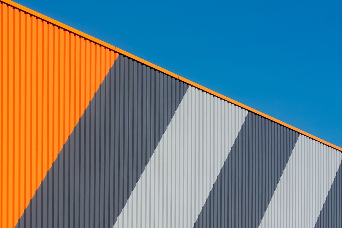 Modern industrial facade clad in orange and grey striped panels under a blue sky