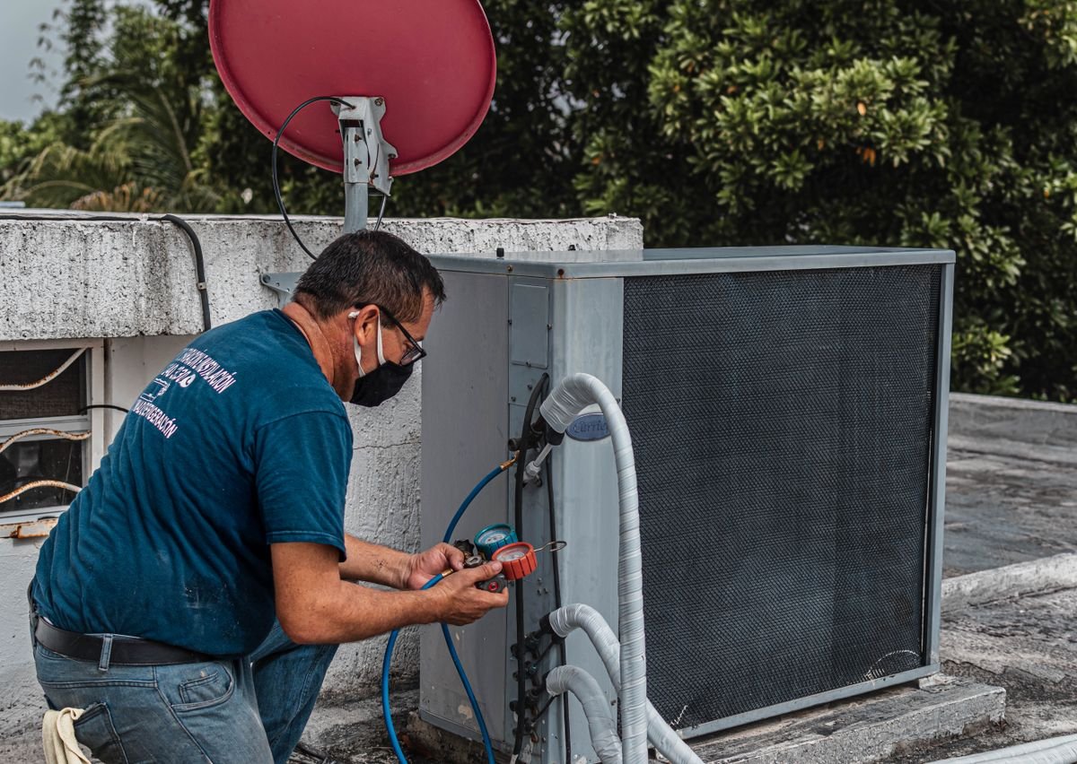 Technician repairing an air conditioner unit outdoors using a manifold gauge