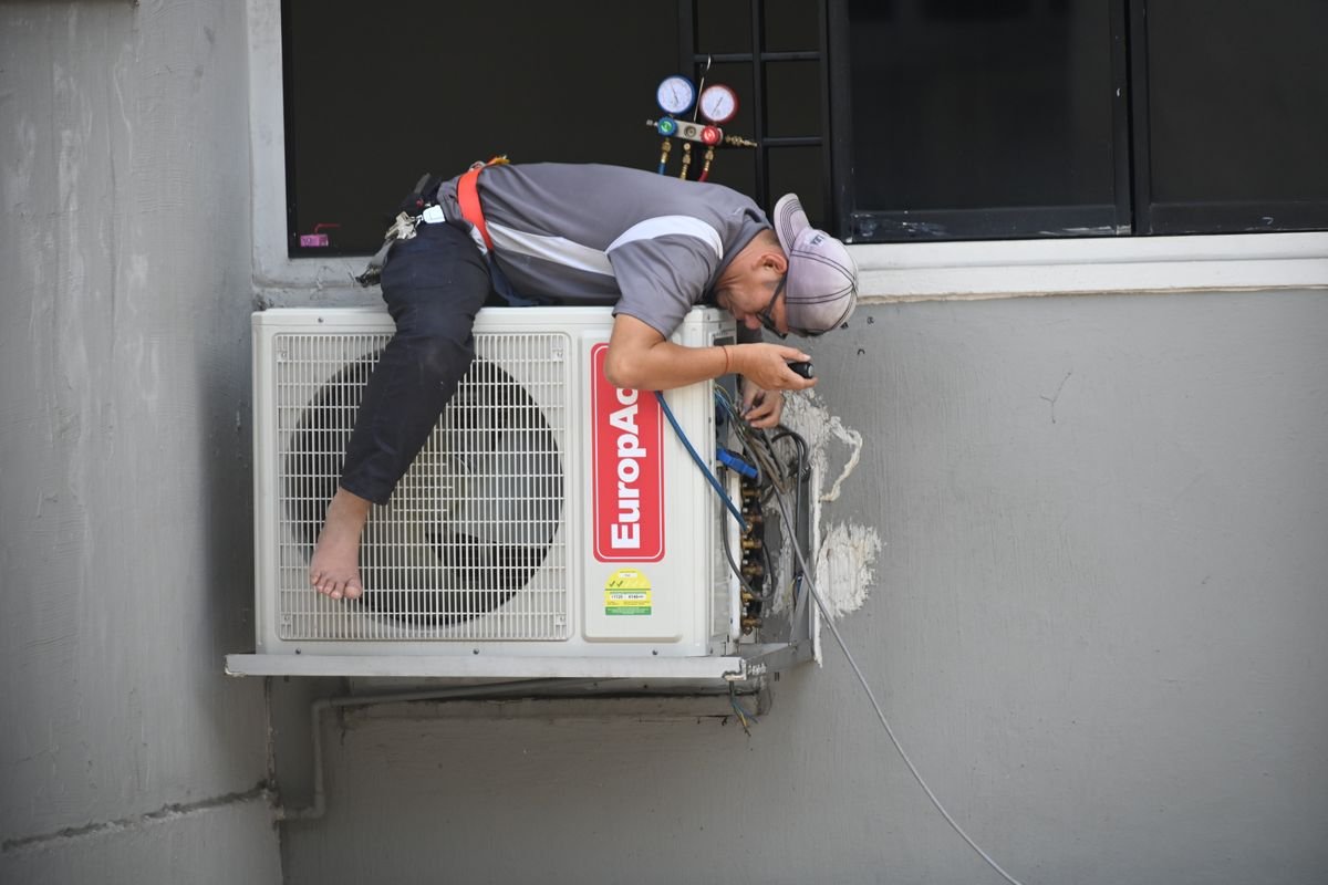 Technician repairing an outdoor air conditioning unit mounted on a building wall