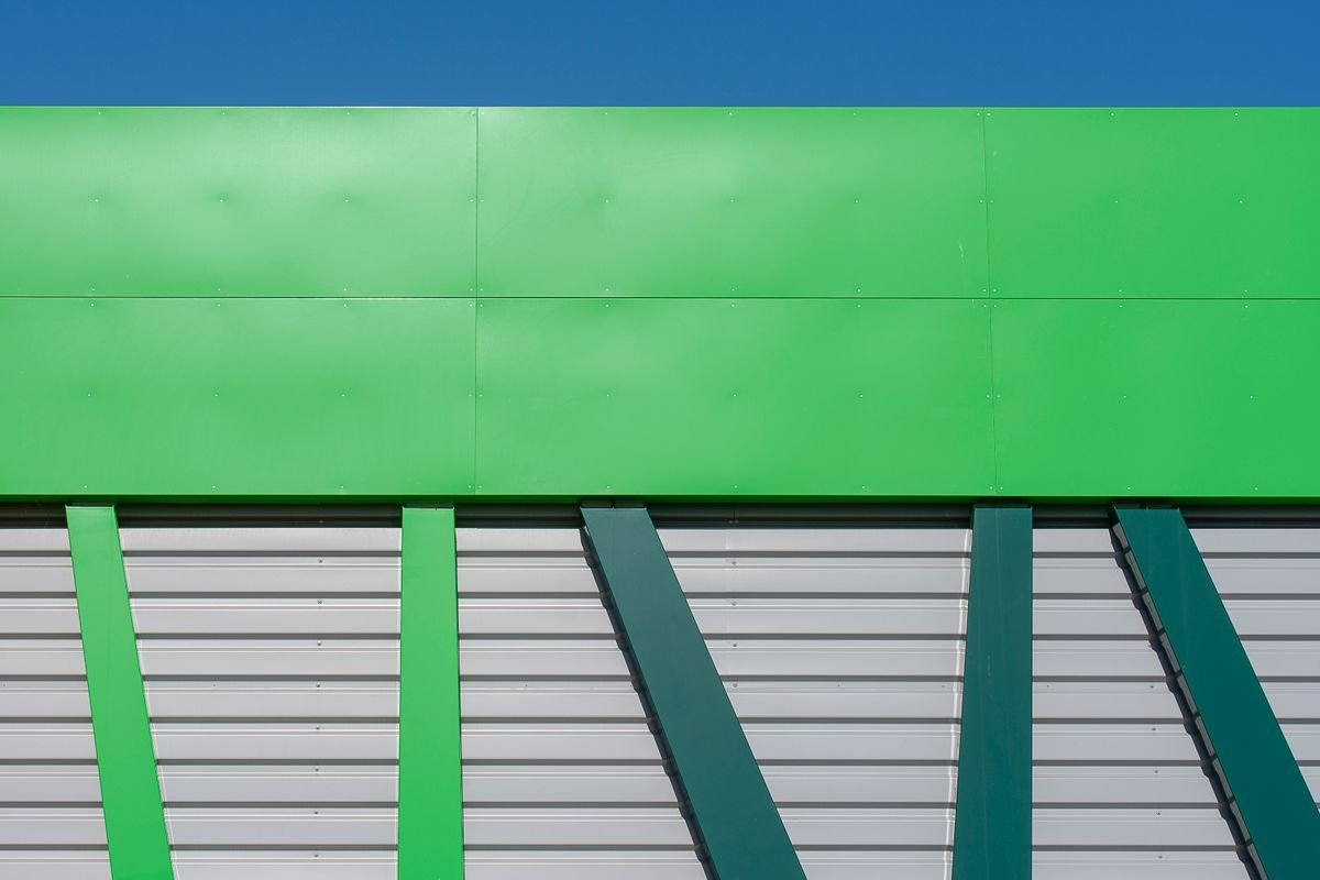 Modern green industrial building facade with a geometric panel design under a blue sky