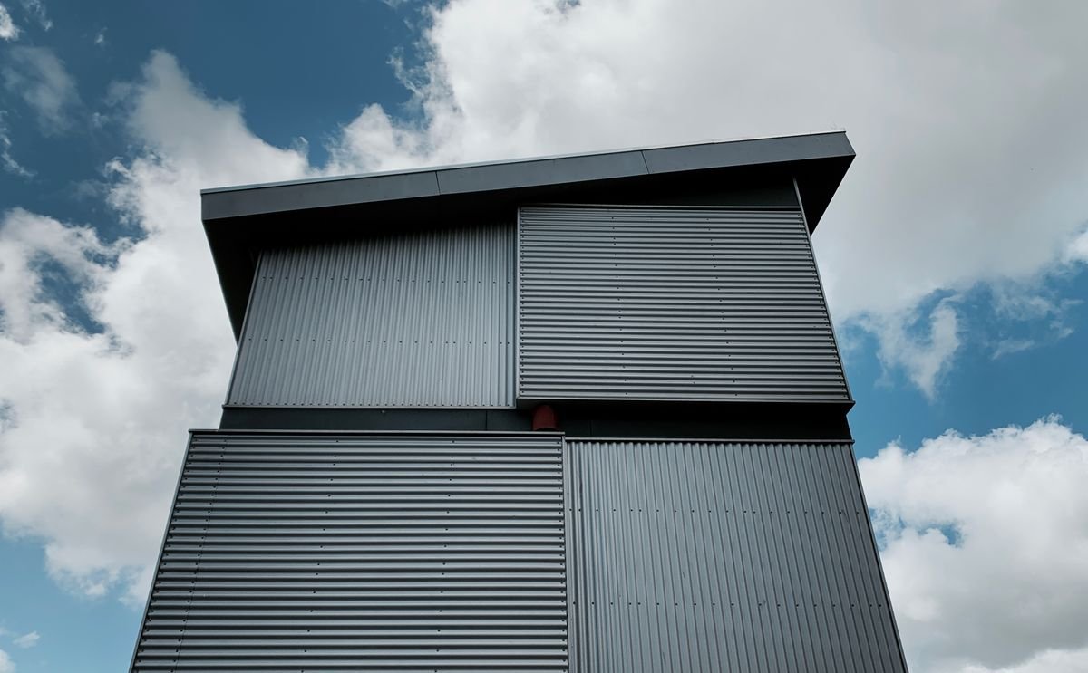 Low-angle view of a sleek modern metal building against a blue, cloud-filled sky
