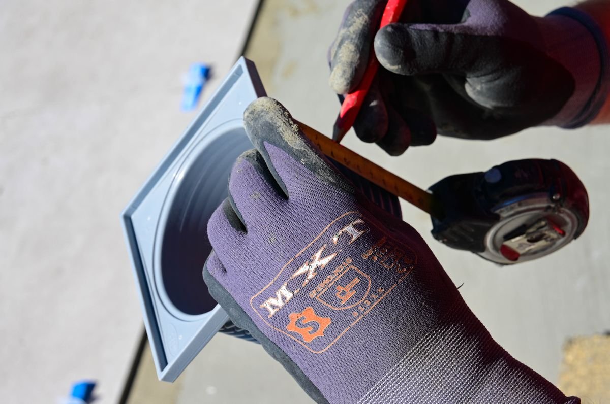 Hands measuring and marking a tile around an inspection access plate