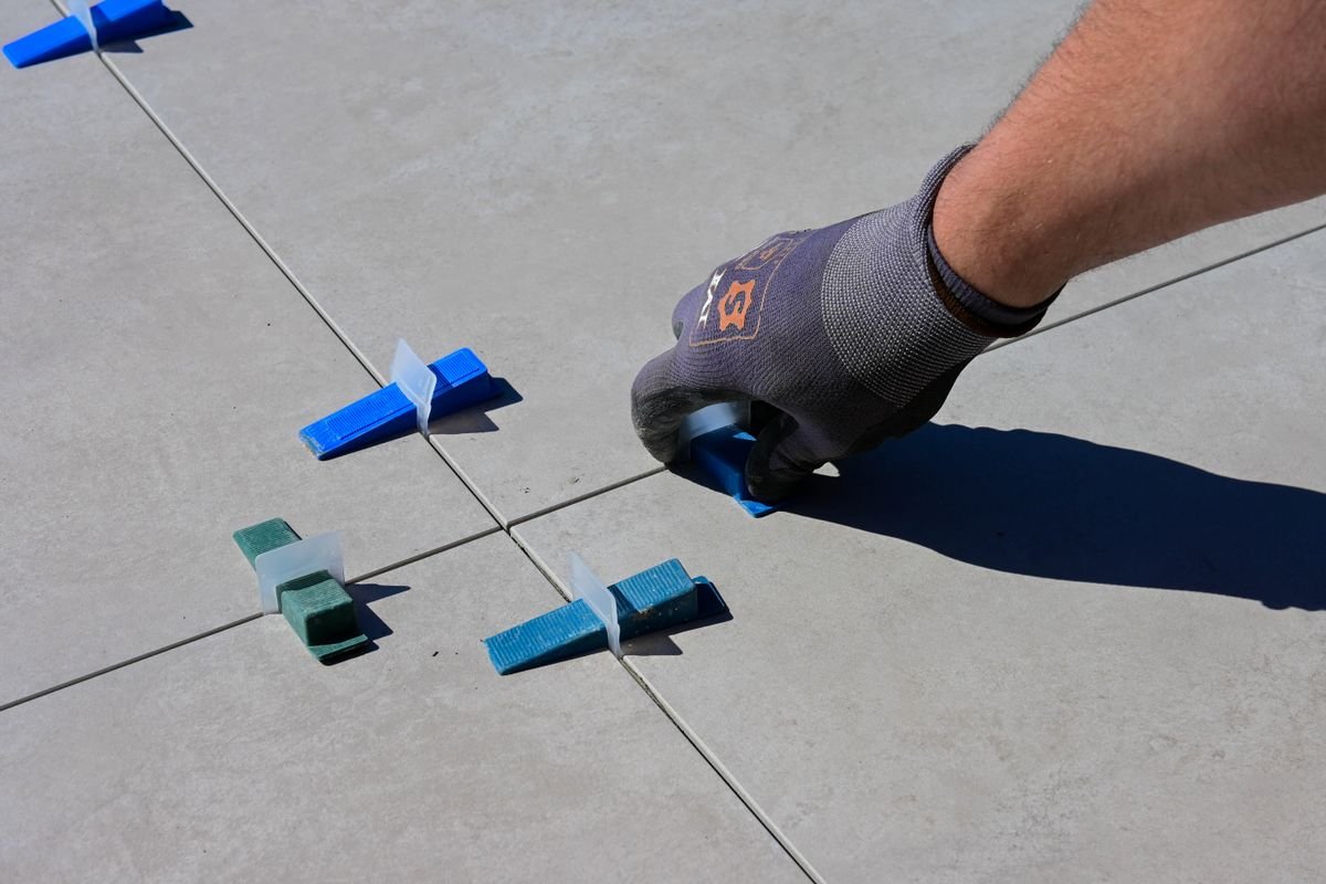 Gloved hand placing blue levelling clips between large porcelain tiles