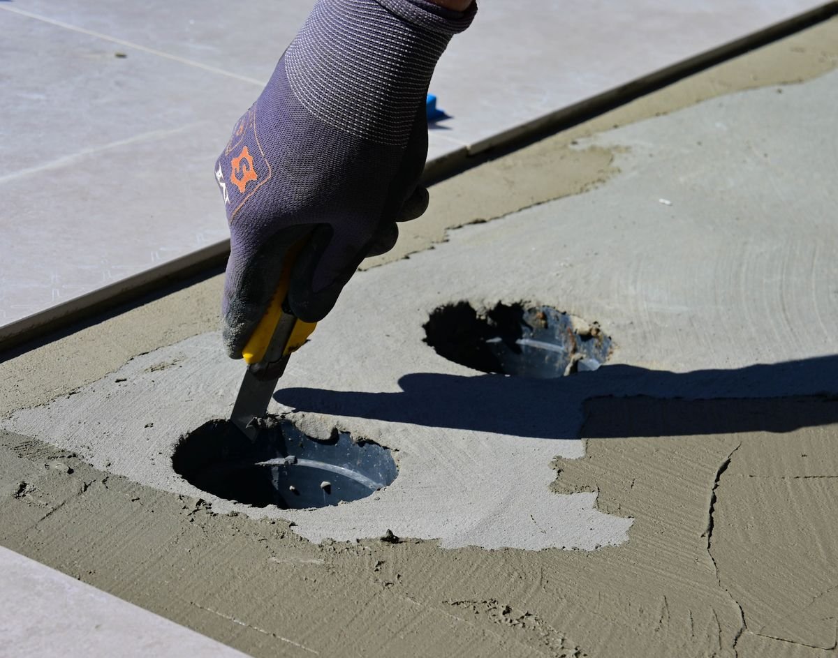 Gloved hand working adhesive around a floor drain opening on large tiles