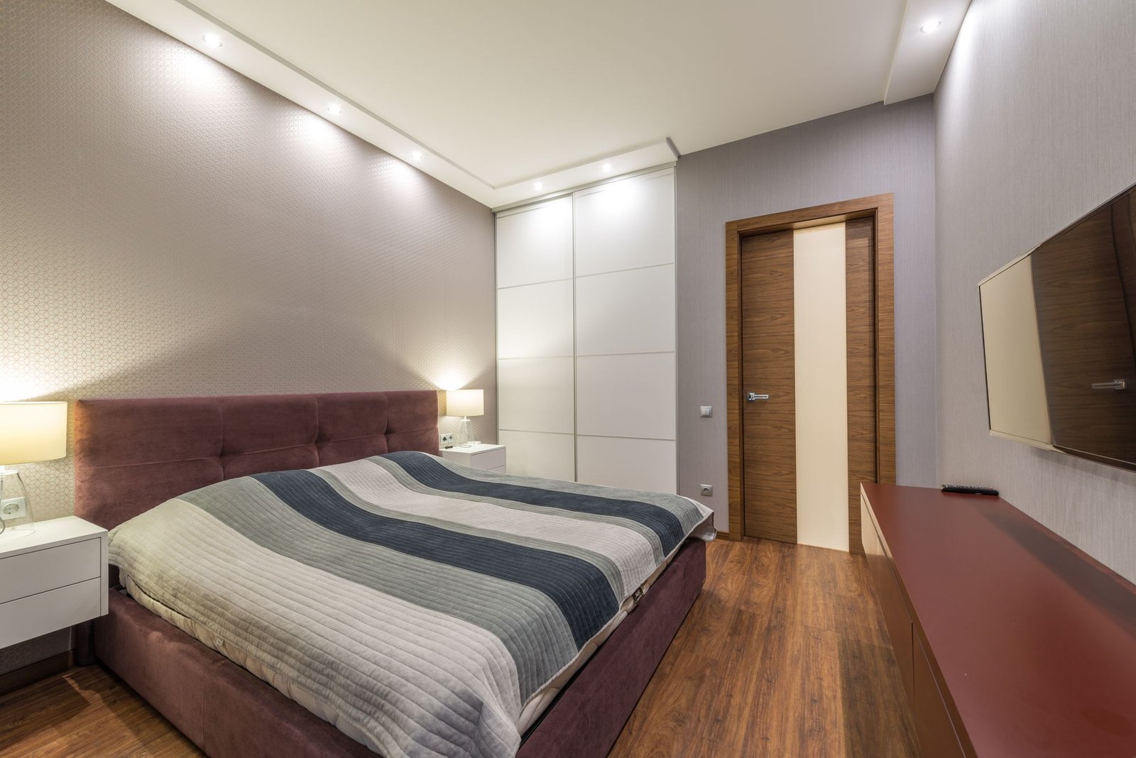 Bedroom with a stepped false ceiling, recessed spotlights, and a burgundy upholstered bed