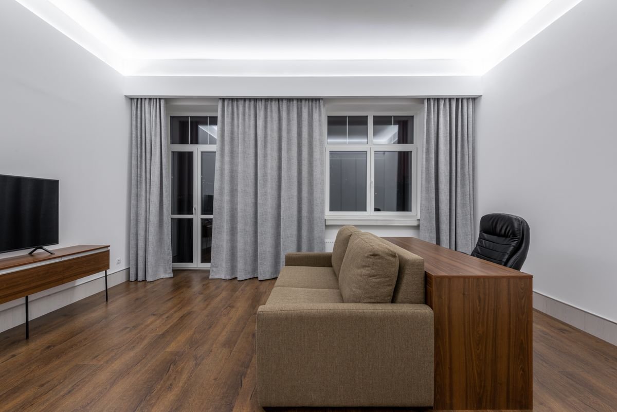 Bedroom lounge area with a cove-lit false ceiling and grey curtains