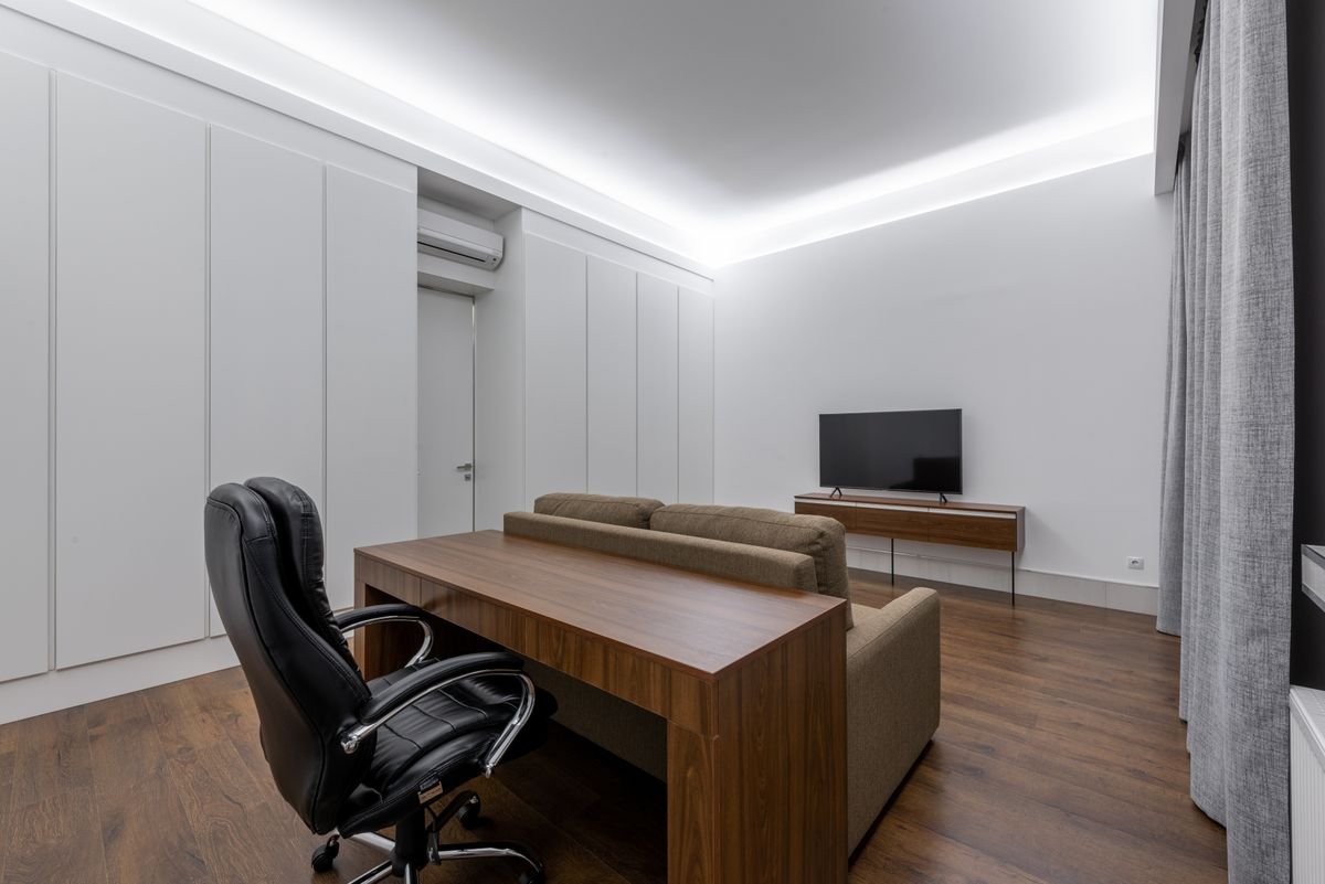 Sitting and study area with a cove-lit ceiling above a desk and sofa
