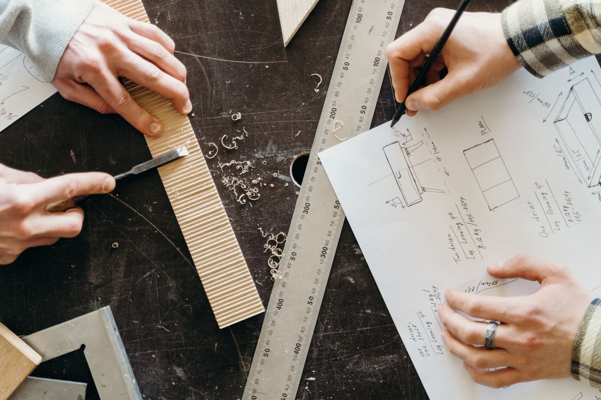Hands designing woodworking projects on paper with rulers