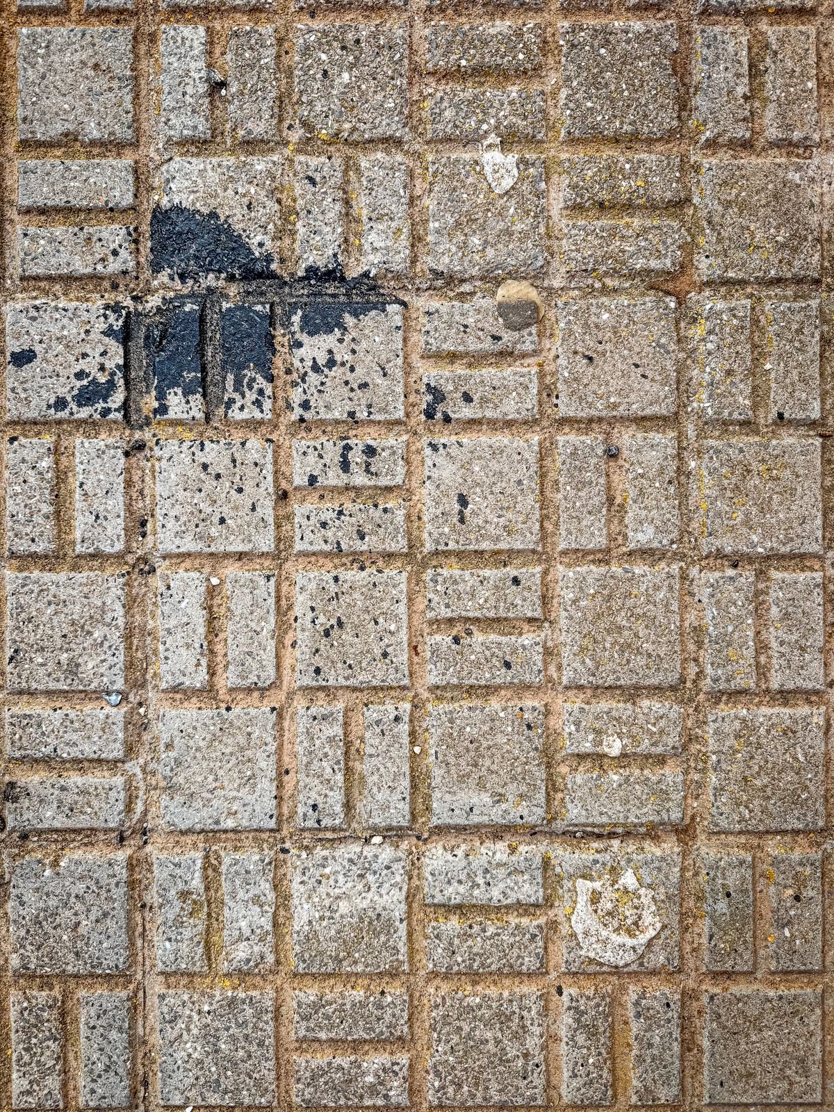 Weathered interlock pavement with dark stains and a patched section