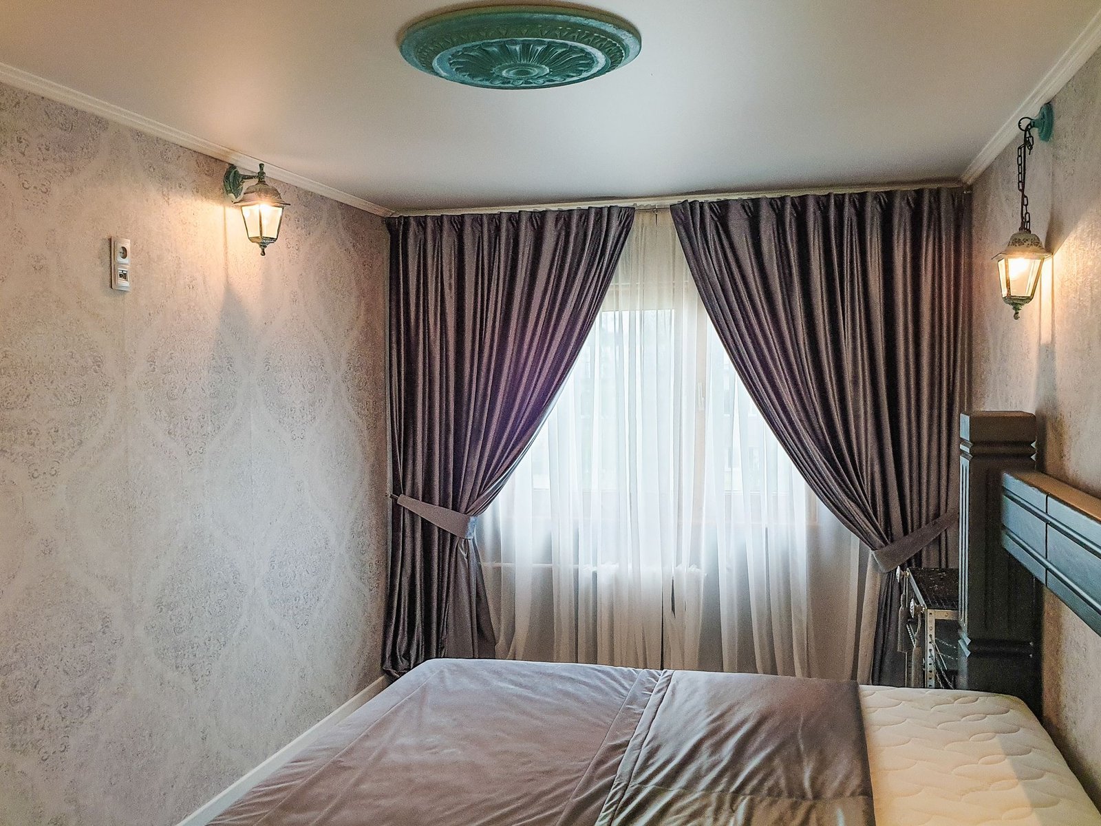 Bedroom finished in elegant patterned wallpaper with draped curtains and a ceiling light