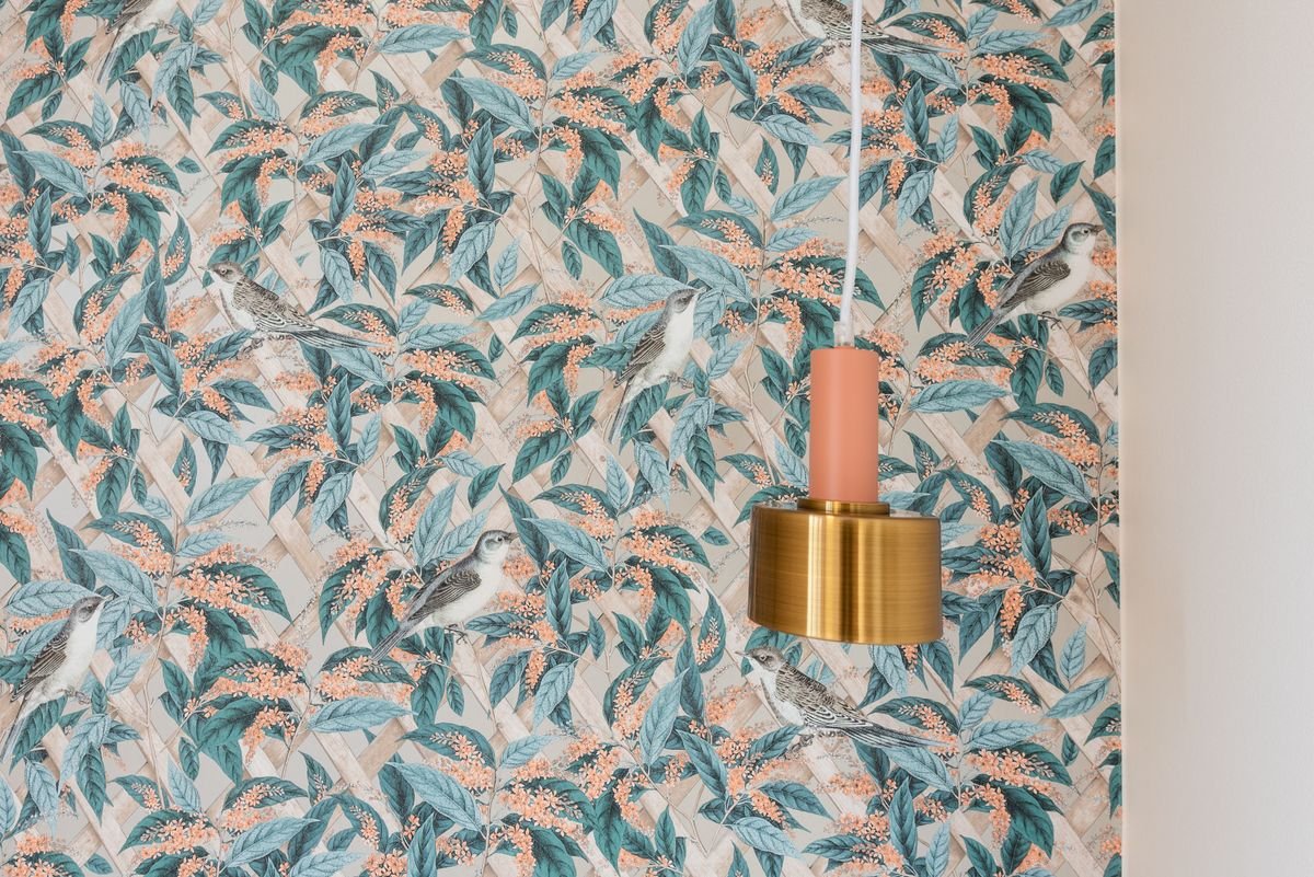 Botanical leaf-pattern wallpaper in teal and blush beside a gold pendant lamp