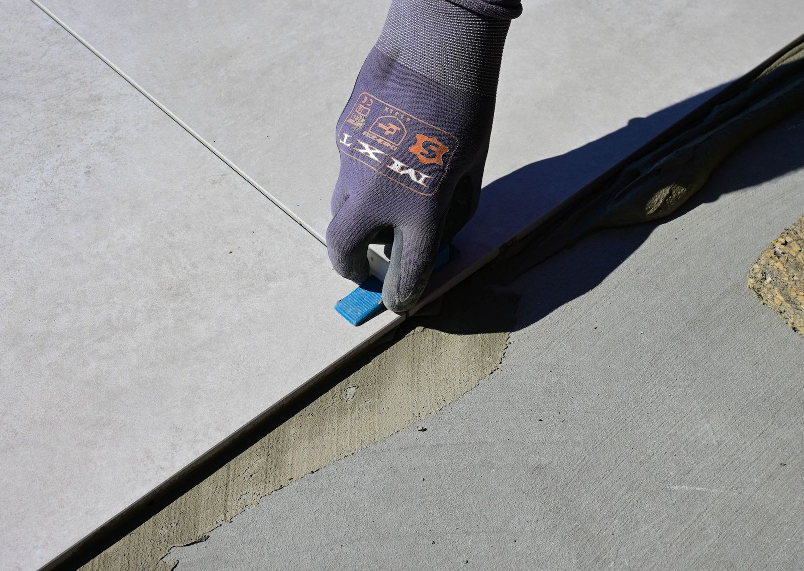 Gloved hand setting a spacer at the edge of a freshly laid ceramic tile