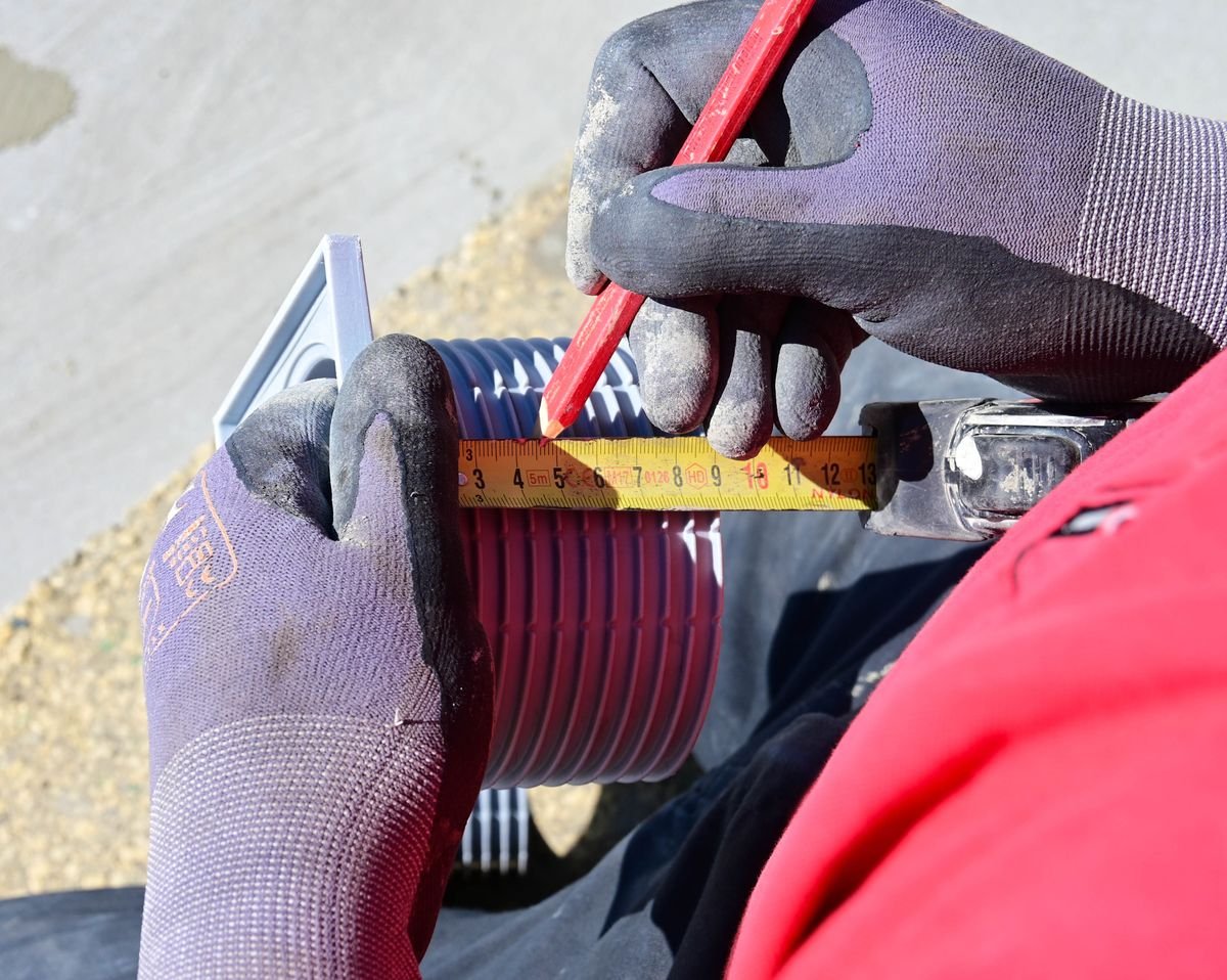 Hands measuring a tile with a tape and marking a cut line