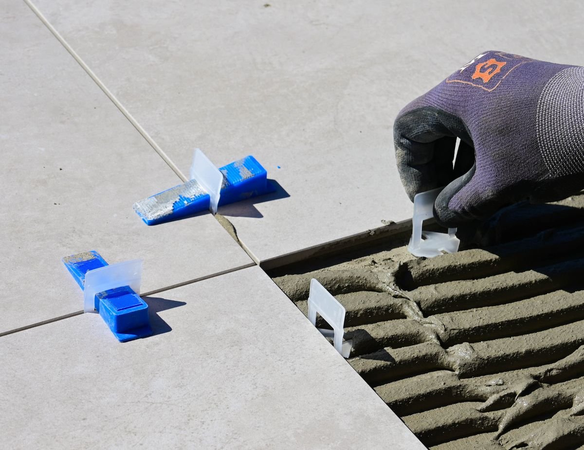 Gloved hand positioning a levelling clip beside trowelled adhesive