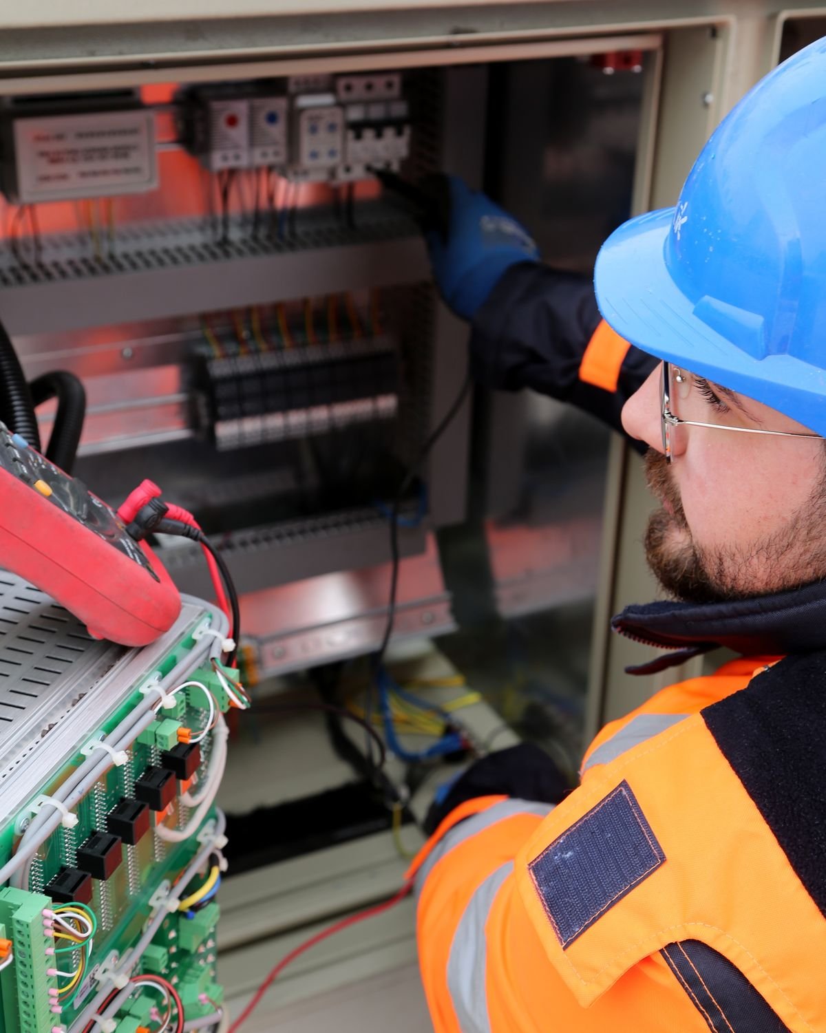 Electrician in hard hat and high-visibility vest inspecting an industrial switchboard
