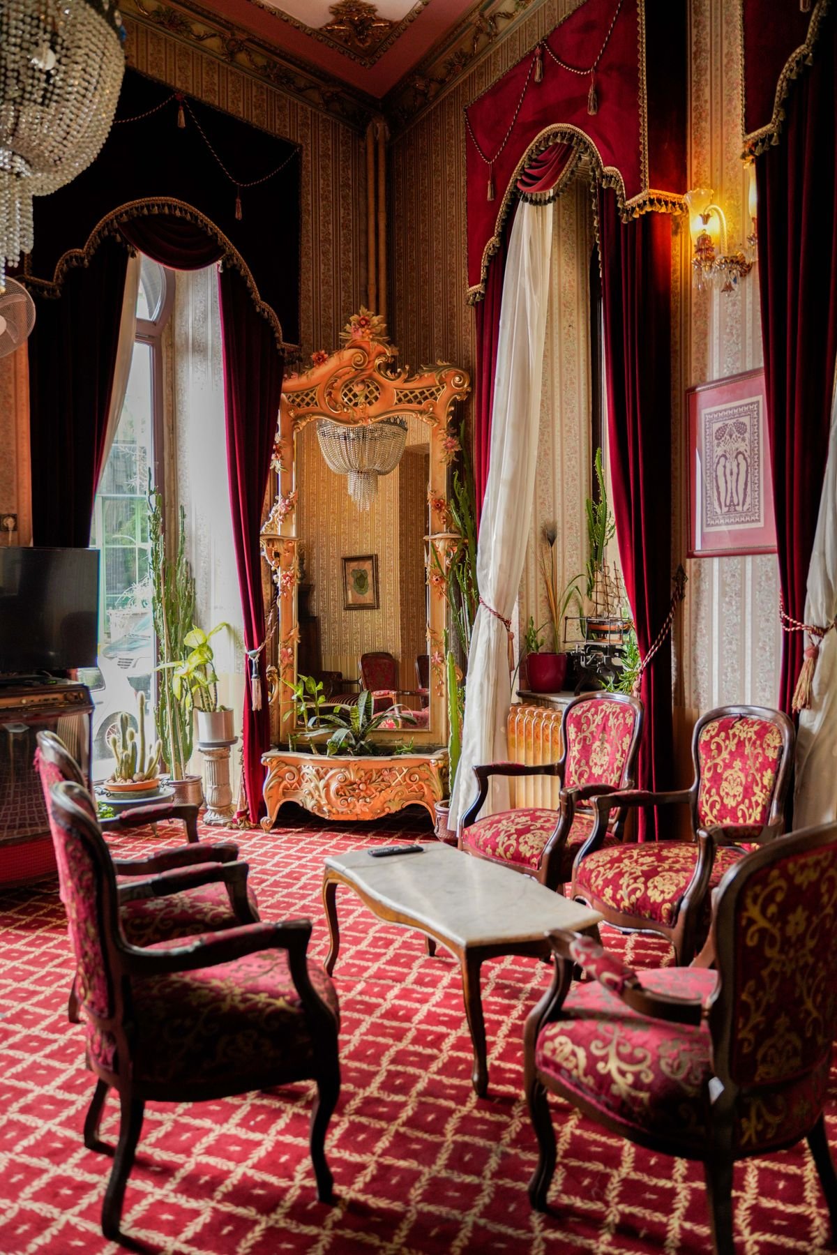 Ornate hotel room with red drapes, carved furniture, and patterned carpet