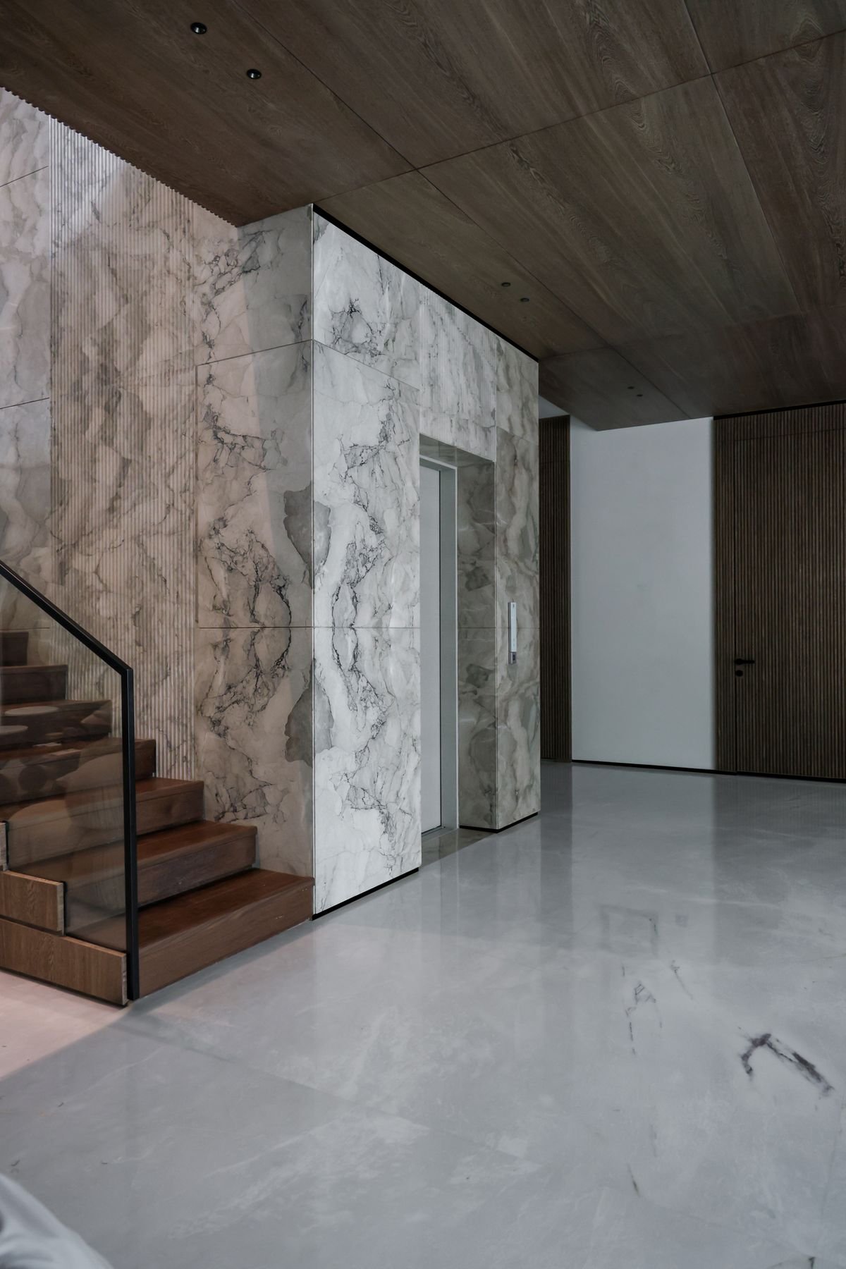 Modern lobby with marble feature walls, a polished floor, and a timber staircase