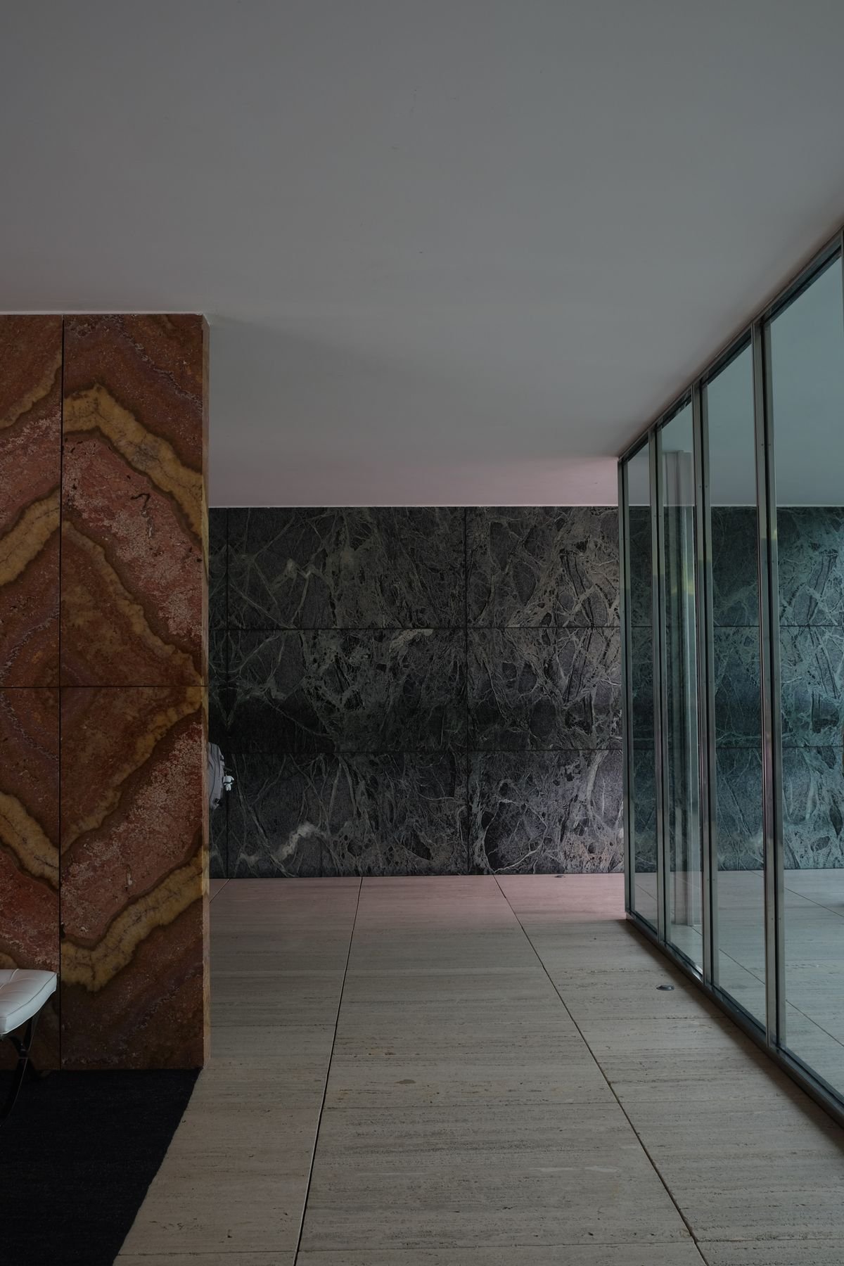 Open pavilion with veined marble walls and a polished floor beside glass doors