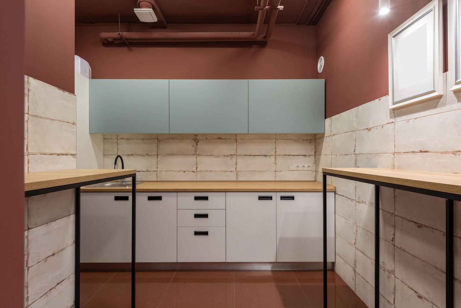 Office kitchenette with painted red-brown walls, white cabinets, and a timber worktop