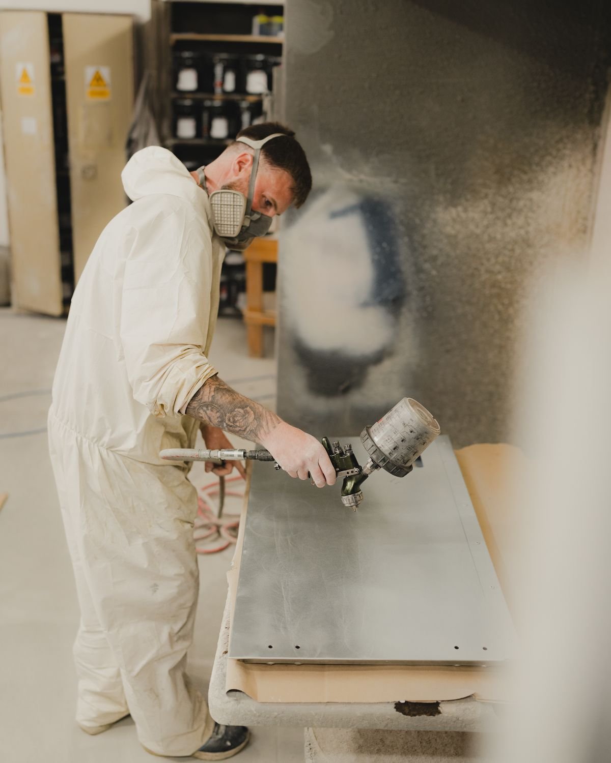 Painter in protective gear spray painting a metal panel in an industrial setting