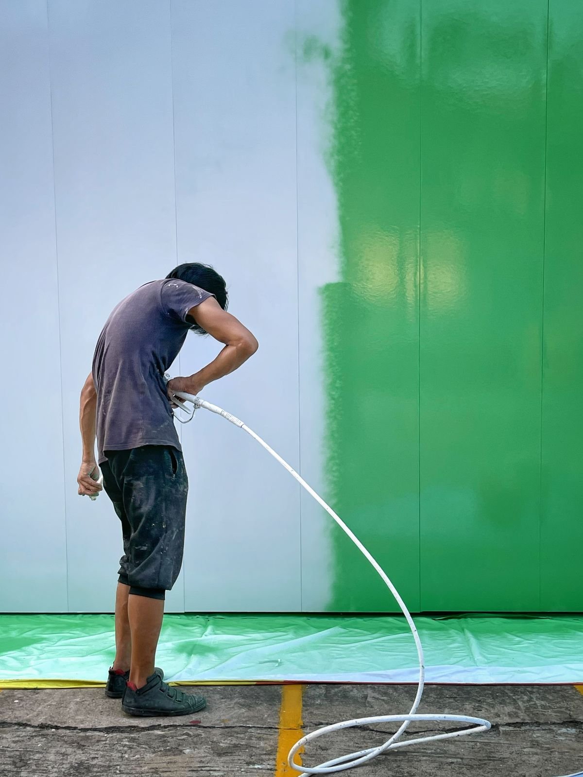 Painter spraying a large wall with the colour changing from white to green