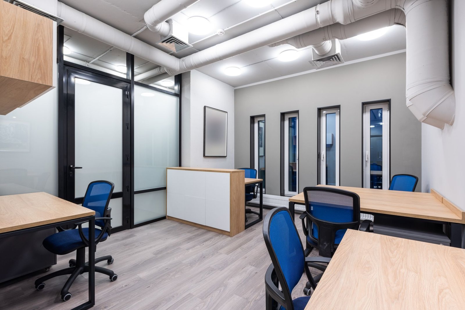 Office with glass-and-black-frame partitions, blue chairs, and bright ceiling lighting