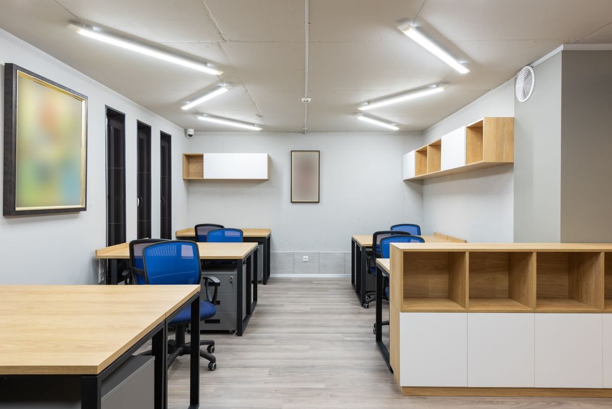 Office interior with desks, shelves, and a framed picture under bright ceiling lights