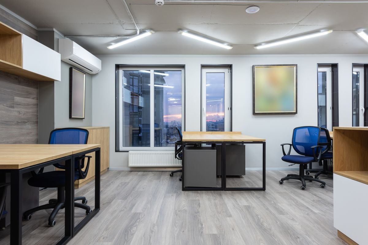 Compact office room with a desk, blue chair, and window light behind a partition