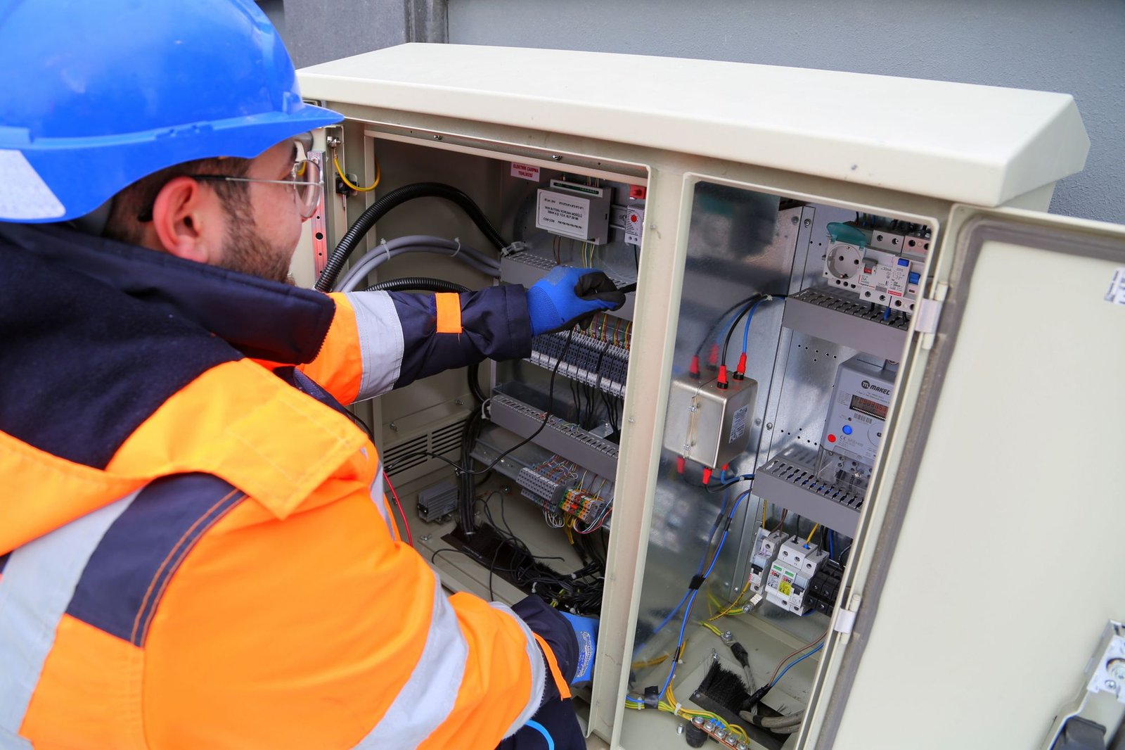 Electrician in hard hat and safety gear inspecting an outdoor electrical control panel