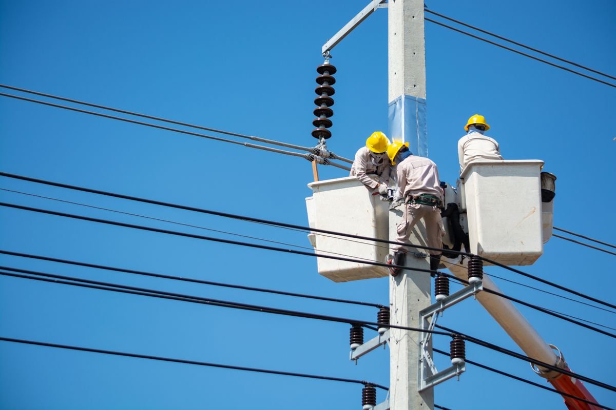 Linemen in safety gear working on overhead power lines from a bucket lift