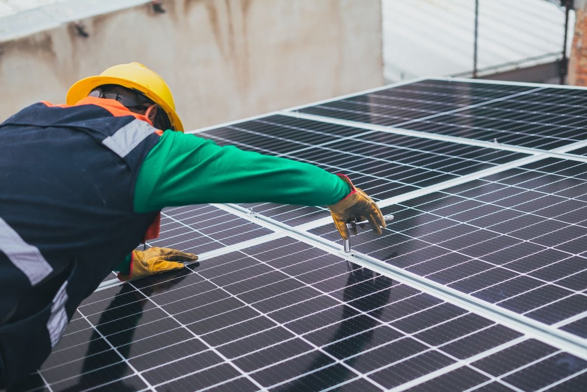Technician in uniform and hard hat installing solar panels on a rooftop