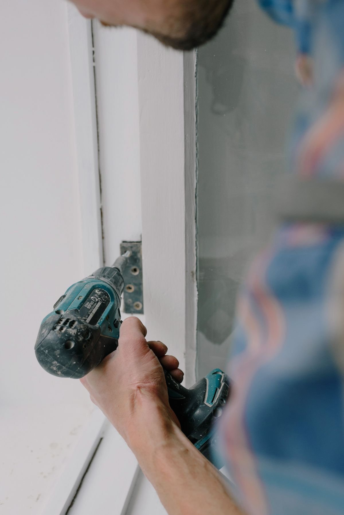 Worker installing a door with screwdriver and metal hinge during renovation