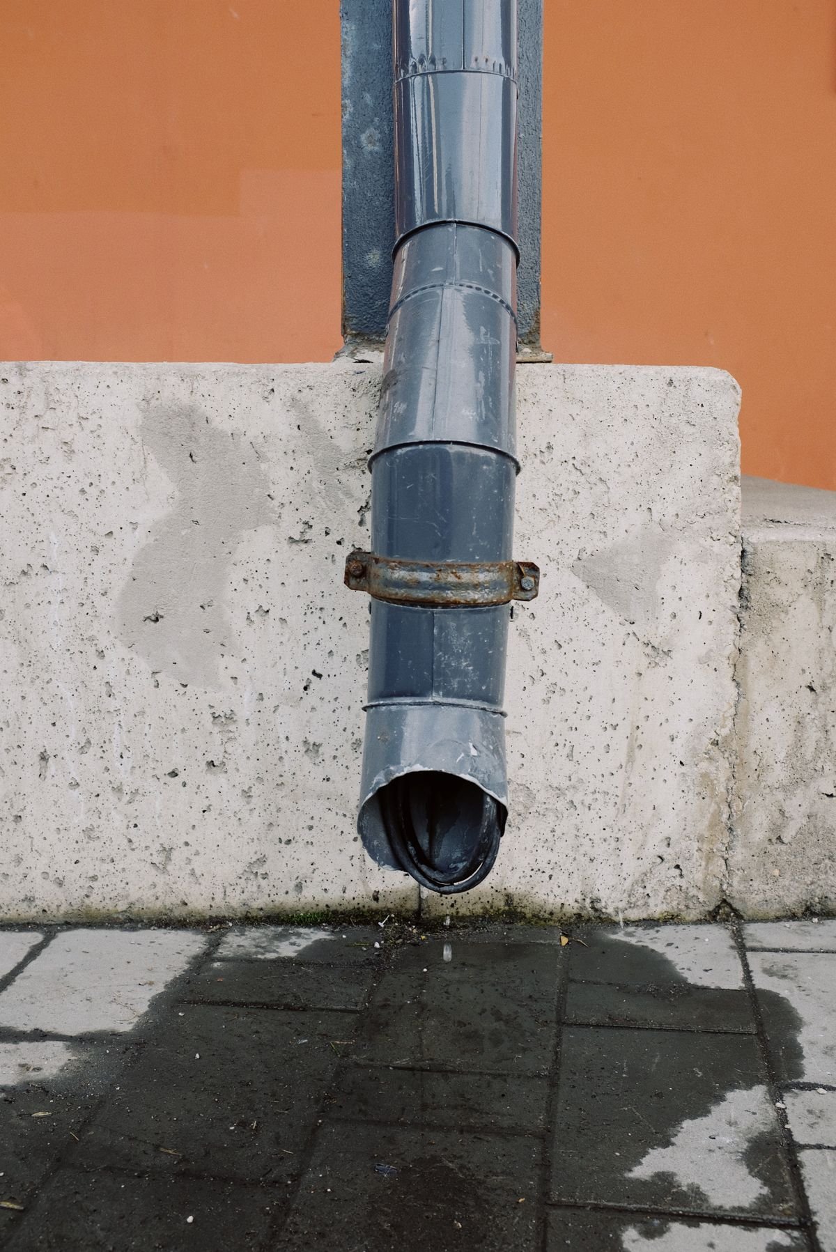 Metal drainage pipe on a concrete wall with visible water runoff