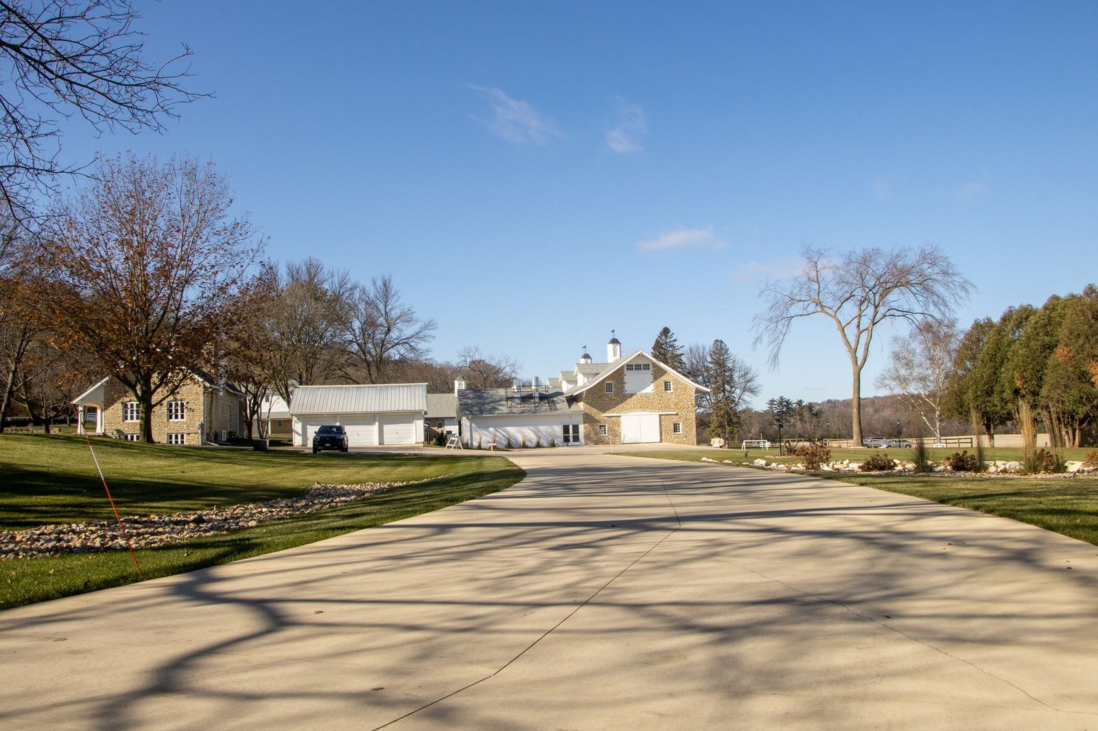 Long smooth paved driveway sweeping toward a rural estate under a clear blue sky