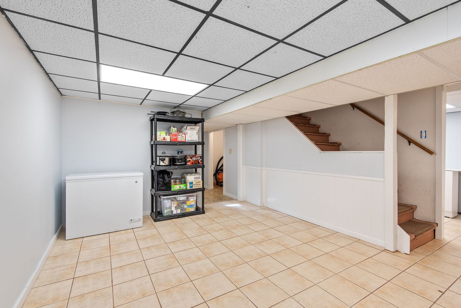 Basement room with a ceiling-mounted light fitting, tiled floor, and storage shelves