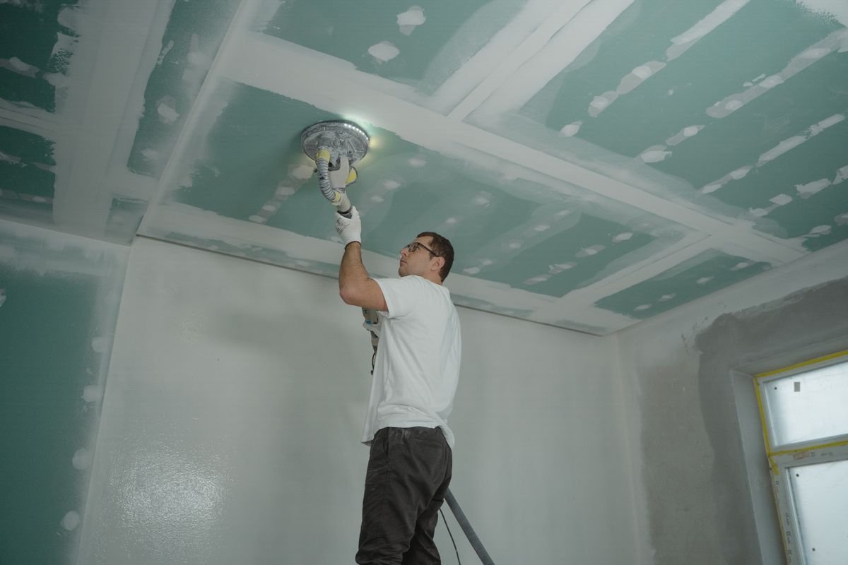 Worker polishing a ceiling indoors during renovation