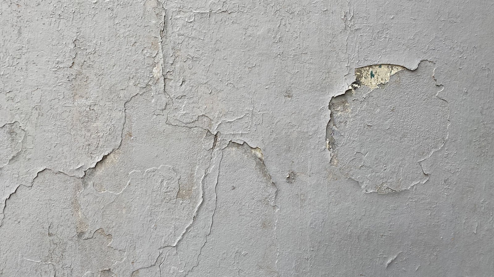 Weathered drywall surface with peeling paint and a patched section