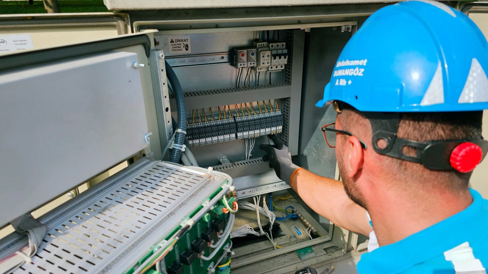 Electrician in safety gear working on an open electrical panel outdoors