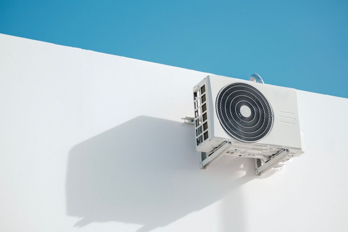 Wall-mounted outdoor air conditioner unit against a clear blue sky