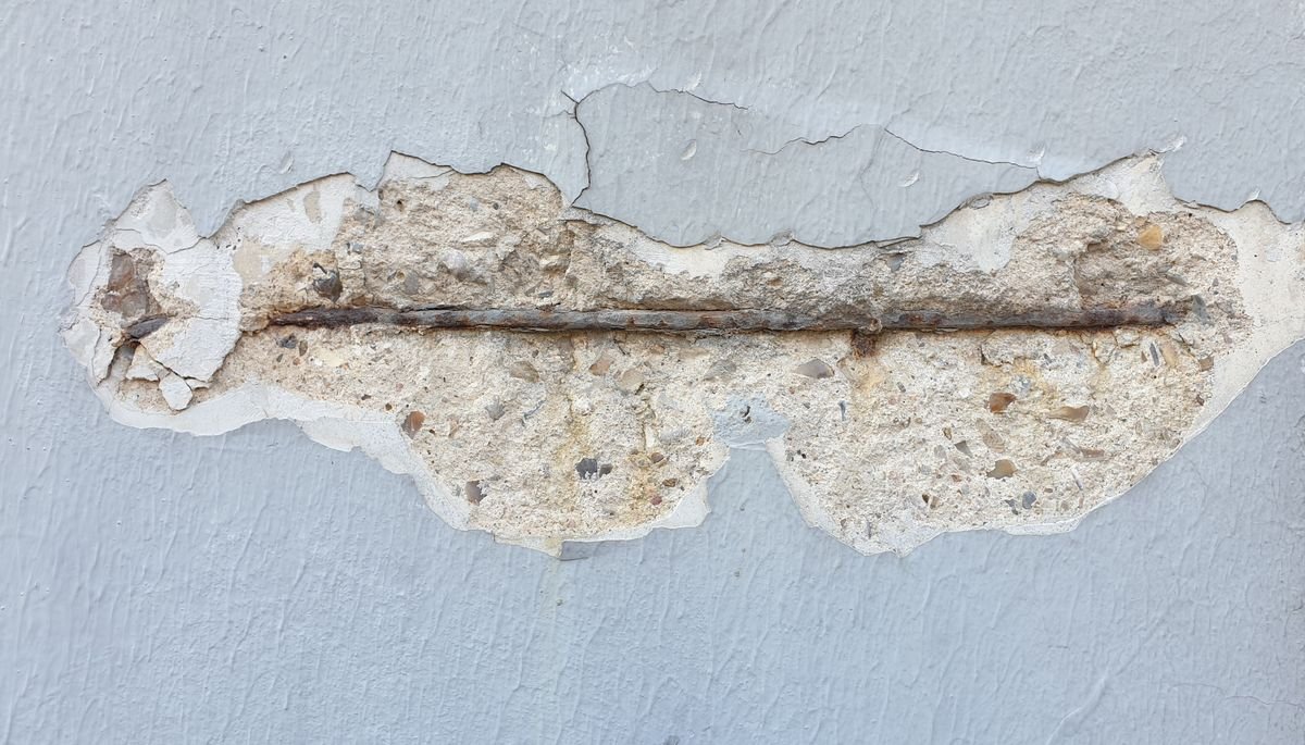 Exposed rusted metal bar where plaster has broken away from a wall