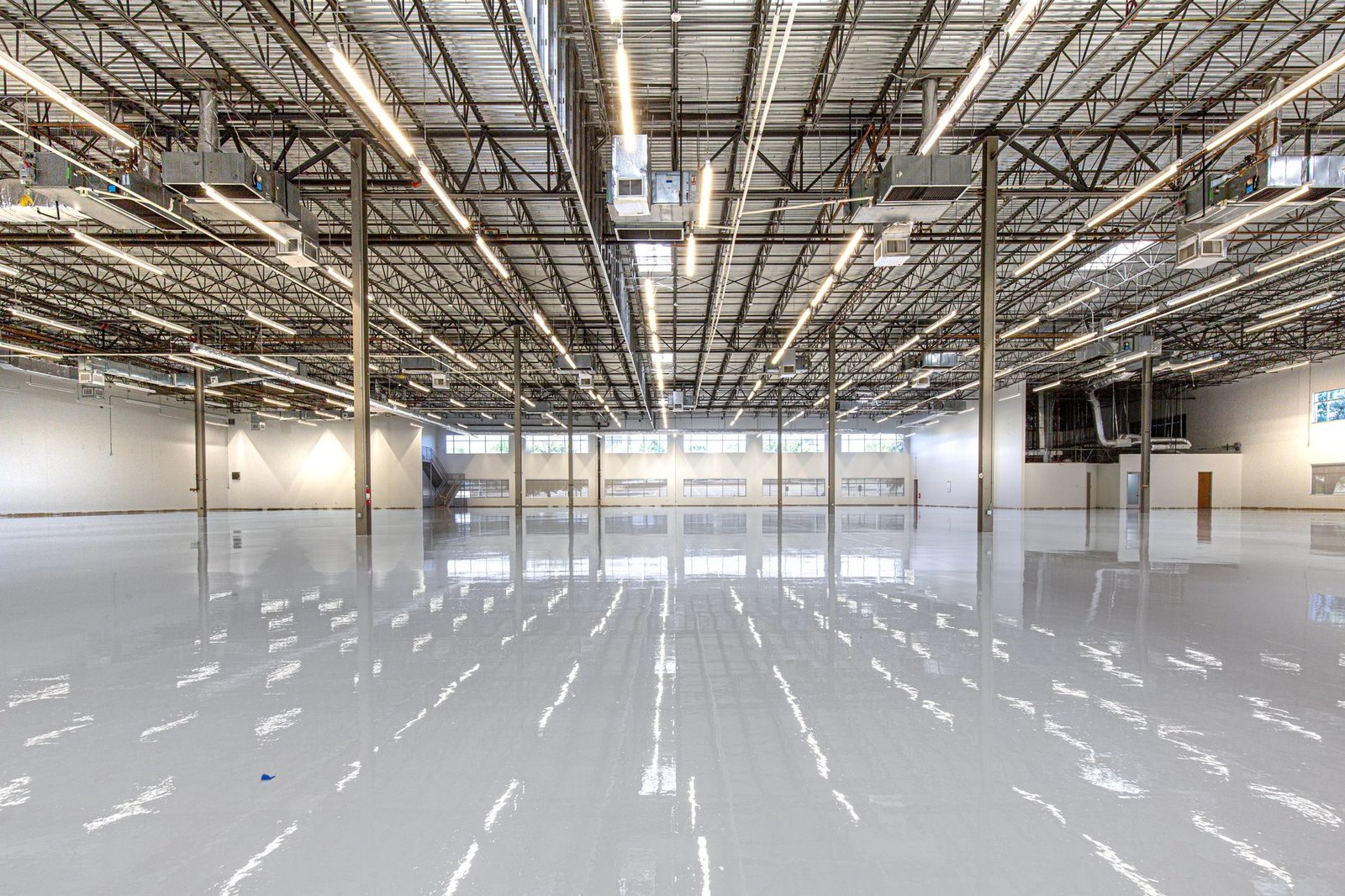 Vast industrial hall with a glossy white epoxy floor reflecting overhead lights