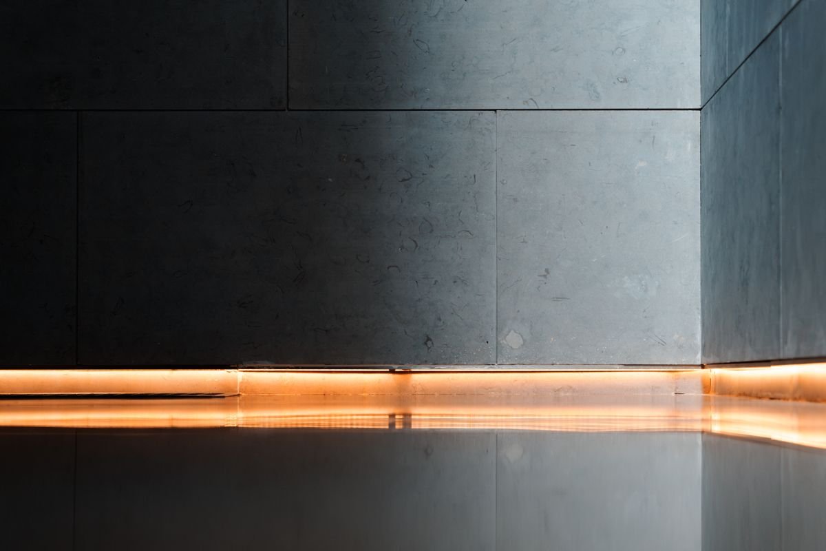 Dark high-gloss floor reflecting an amber strip of light along the wall